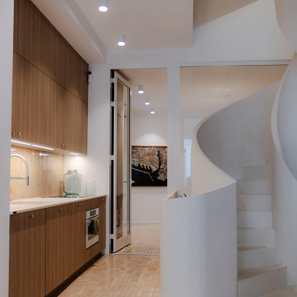 Cuisine avec bejmat émaillé beige posé au sol et en crédence, façades en noyer et escalier en colimaçon