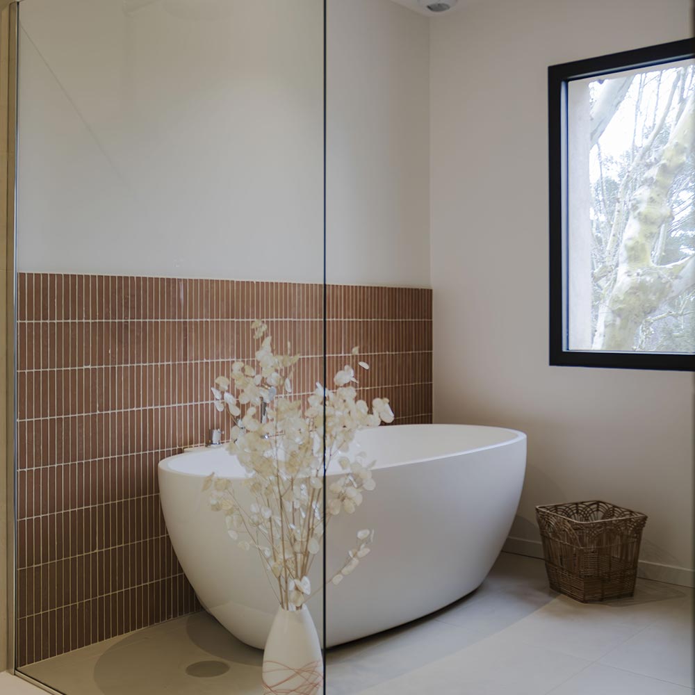 Salle de bain : carrelage effet pierre bouchardée blanc Bera White, relief minéral et lumière douce.